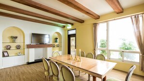 A dining room with a wooden table and chairs, a television on a shelf, and a window with curtains. - Glen Ivy (Hualien City)