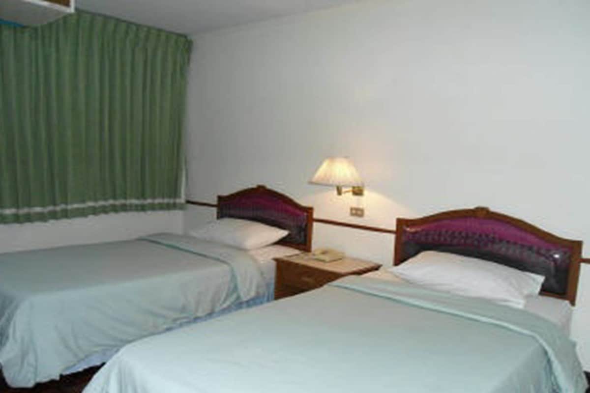 A room with two single beds, a nightstand with a lamp, and a green curtain.
