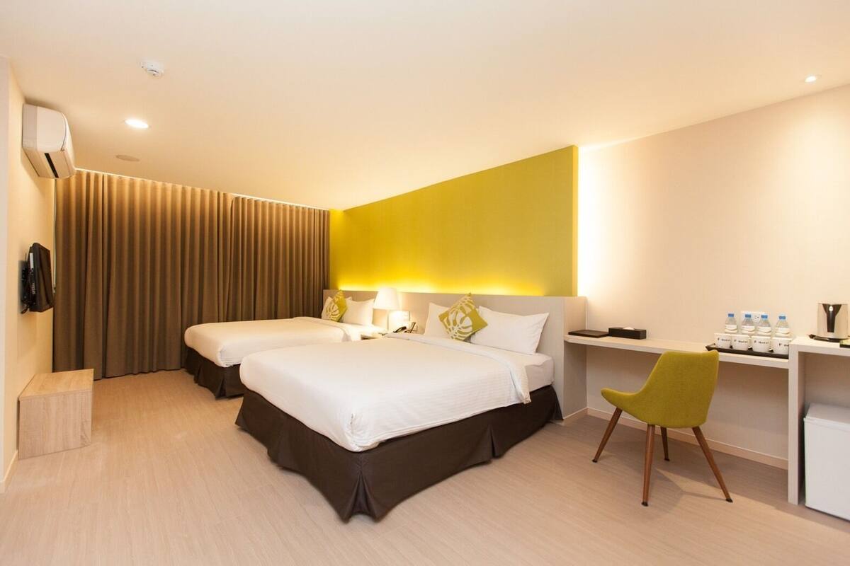Ein Hotelzimmer mit zwei Betten, einem Schreibtisch, einem Stuhl, einer Klimaanlage und einem Wasserspender.