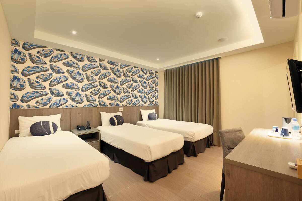 Ein Hotelzimmer mit drei Betten, einem Schreibtisch und einer Wand mit Muster.