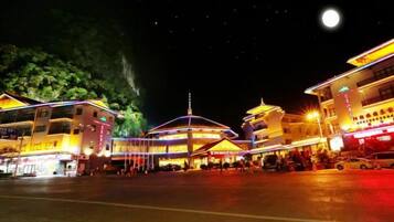 Un edificio tradicional con una cúpula central y un techo al estilo pagoda, rodeado de construcciones modernas con señalización iluminada.