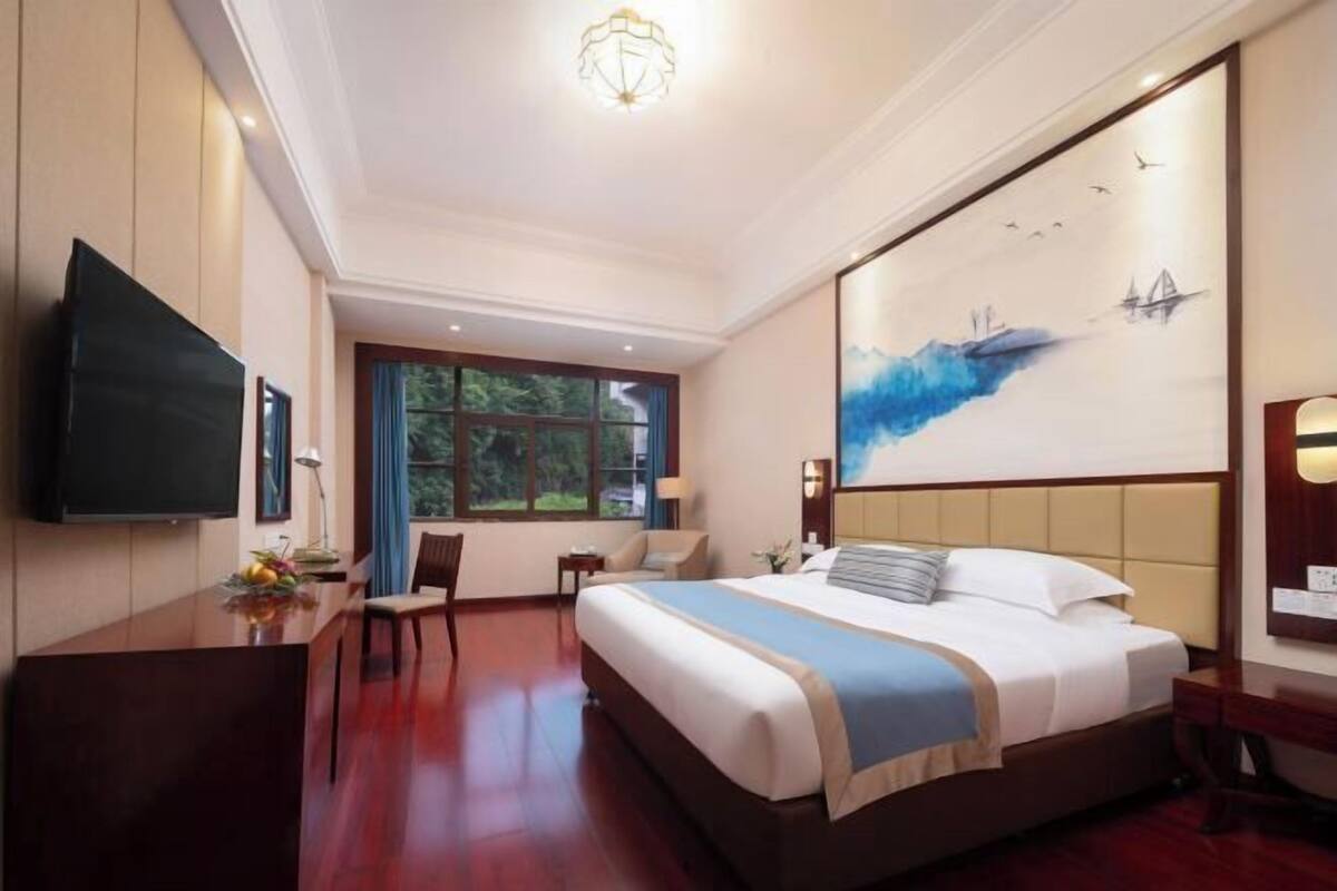 Habitación de hotel con cama, escritorio, televisión y un amplio ventanal.