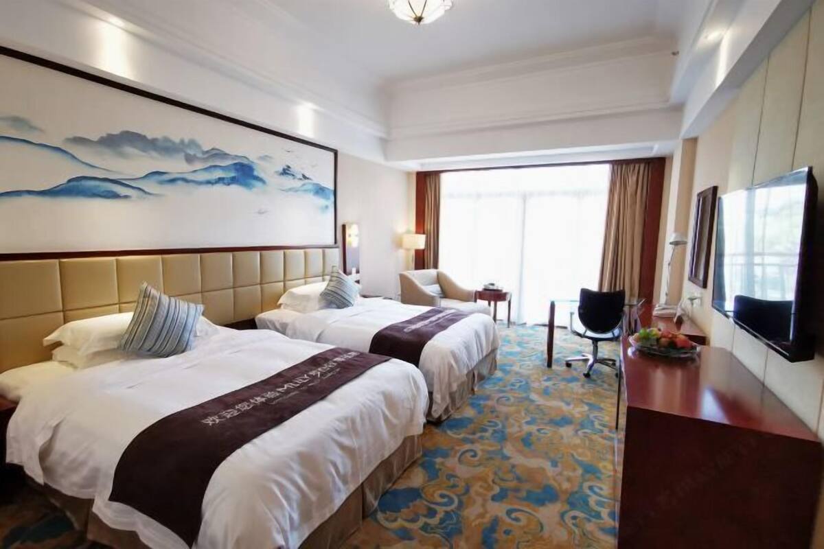 Habitación de hotel con dos camas, un escritorio, una silla, un televisor y un cuadro en la pared.