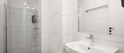 Un baño moderno con ducha de vidrio, inodoro blanco y lavamanos con espejo.