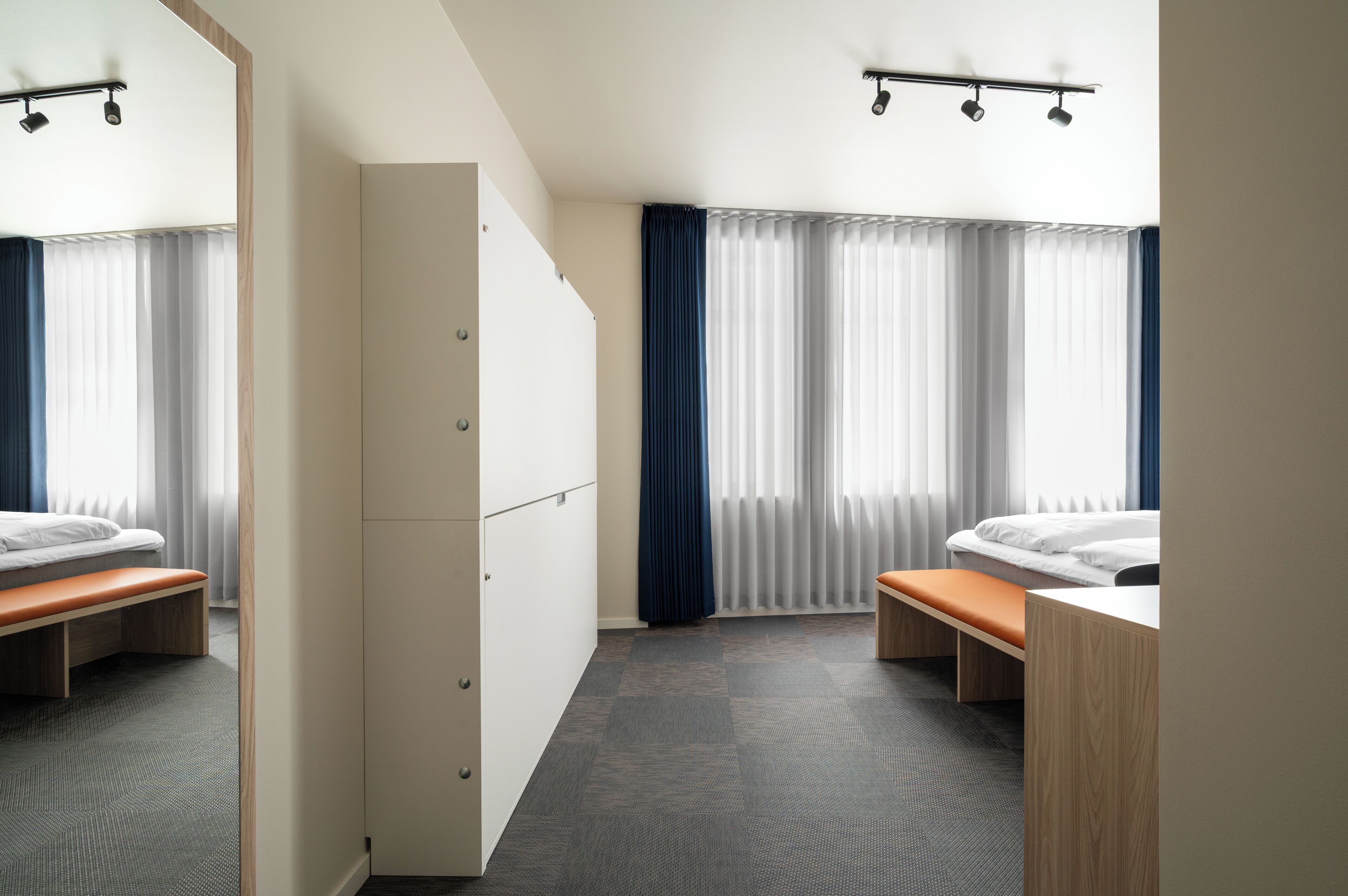 A hotel room with a bed, a bench, a wardrobe, and a window with curtains.