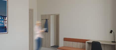 Una habitación de hotel moderna con una cama, un escritorio, una silla, un banco y una puerta.