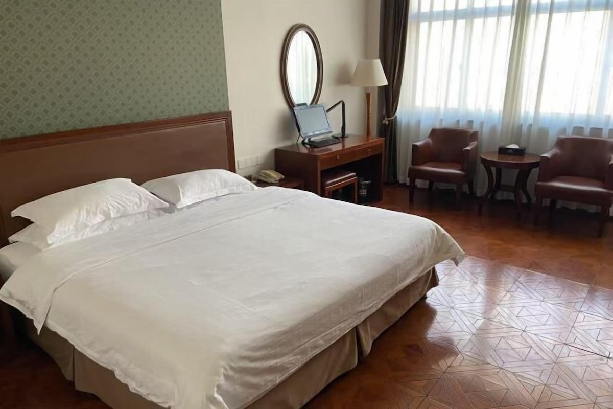 A hotel room with a large bed, a desk with a laptop, a mirror, two chairs, and a small table.