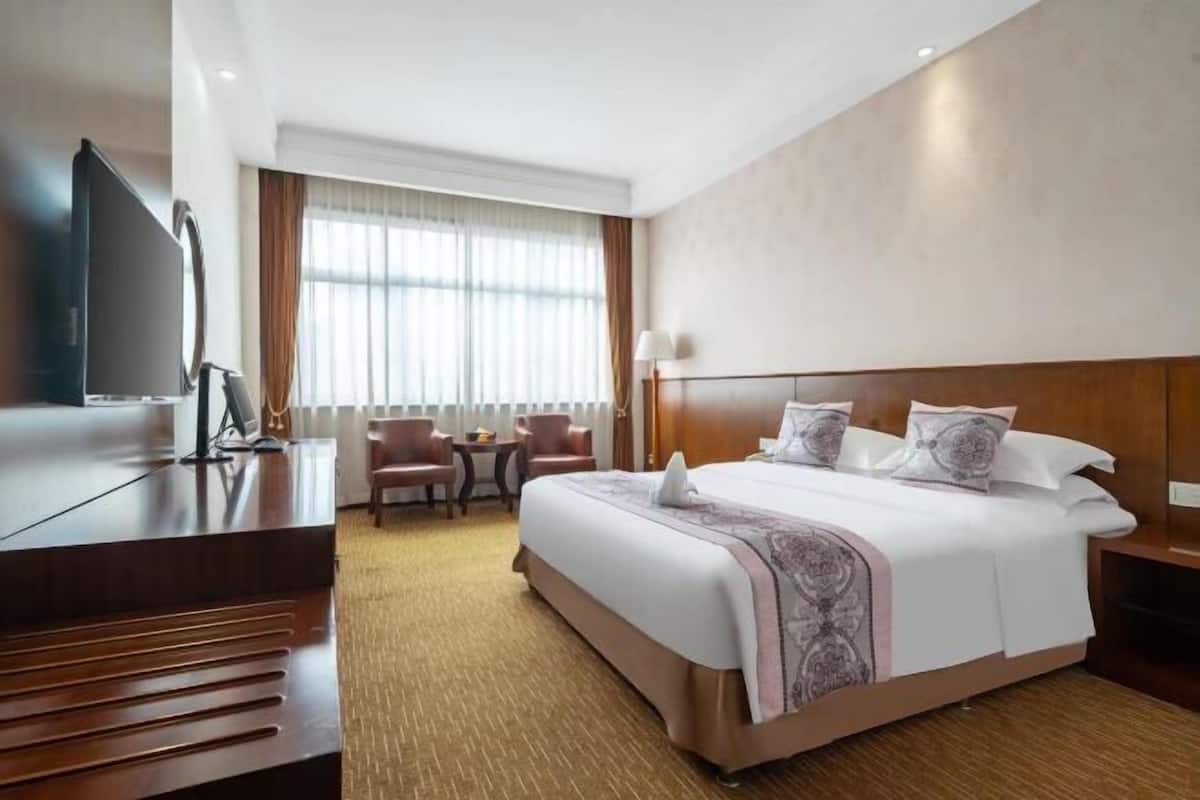 A hotel room with a bed, a desk, a television, a window with curtains, and a small table with chairs.