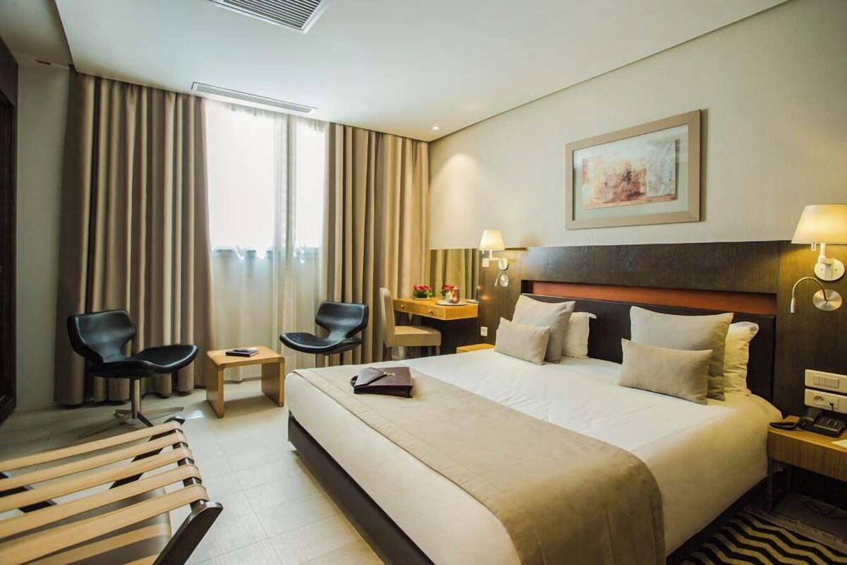 A hotel room with a large bed, two chairs, a desk, and a small table.