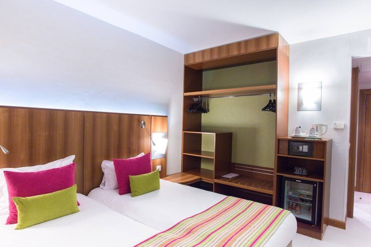Habitació d'hotel amb llit, taules de nit, armari, mirall i mini-nevera.