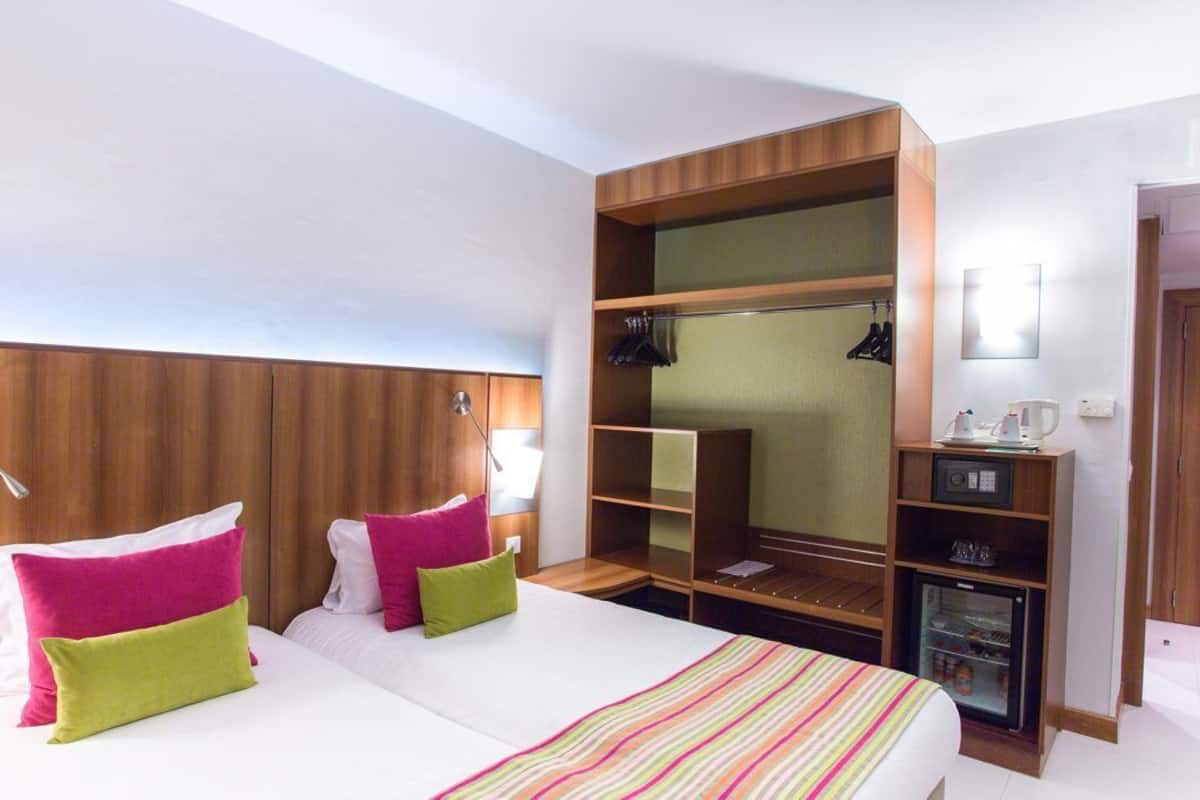 Ein Hotelzimmer mit Bett, Nachttischen, Kleiderschrank, Spiegel und einer Minibar.