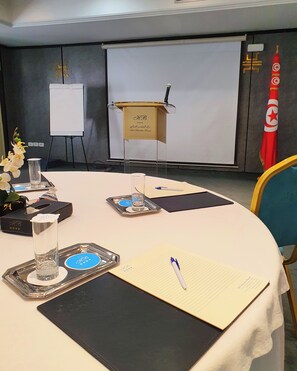 A conference room with a podium, a whiteboard, a flag, and a table with documents and glasses. - Le Belvedere (Tunis)