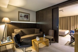 A modern hotel room with a sofa, a wooden coffee table, a chair, a bed, and a desk with a lamp. - Le Belvedere (Tunis)