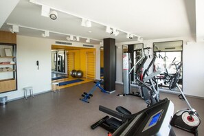 A gym with exercise equipment, a mirror, and a yellow door. - Le Belvedere (Tunis)