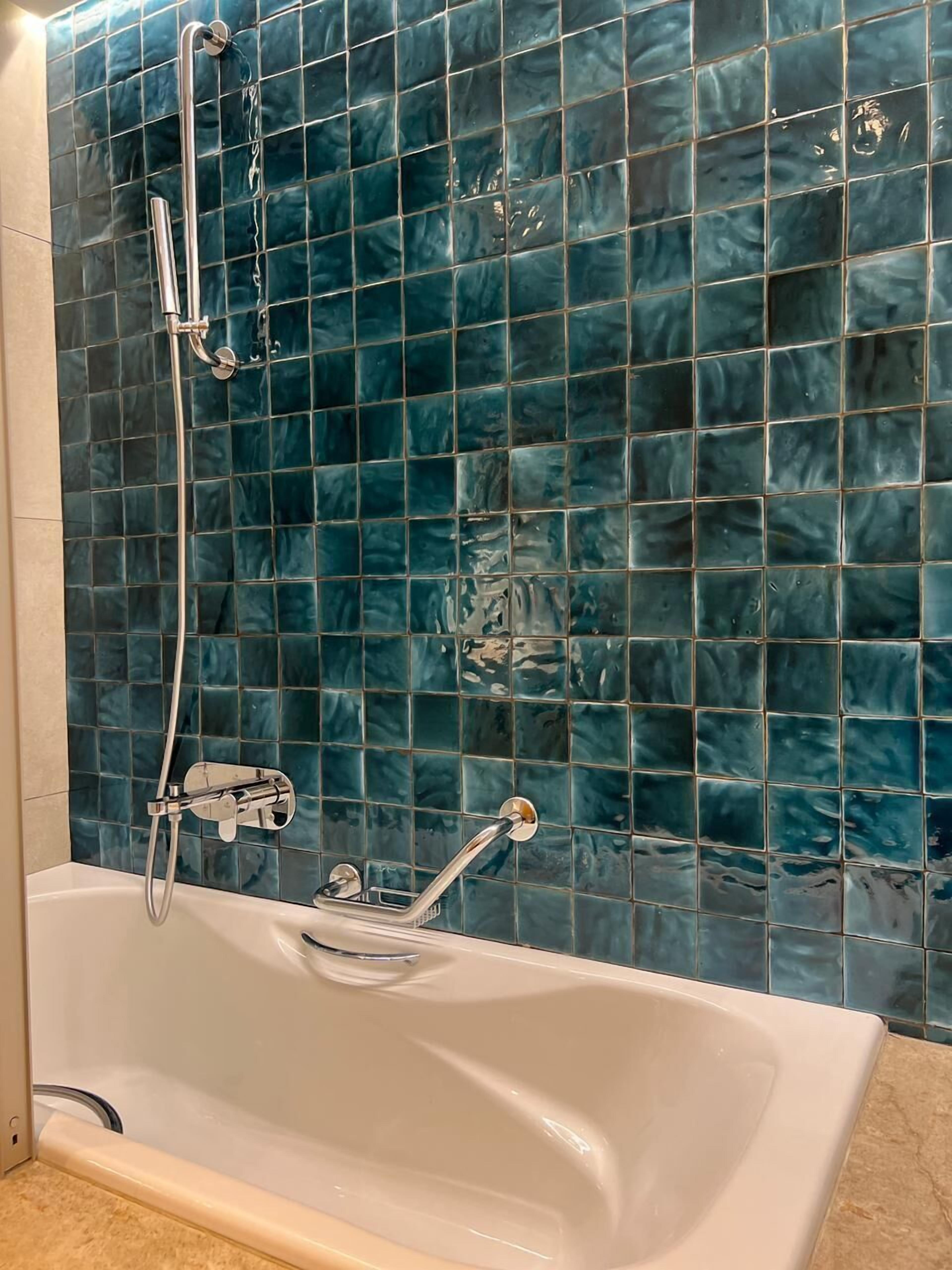 A bathtub with a shower head and faucet, a tiled wall, and a beige floor.