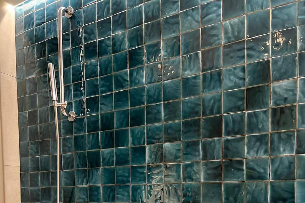 Une baignoire équipée d’une pomme de douche et d’un robinet, un mur carrelé et un sol de couleur beige.