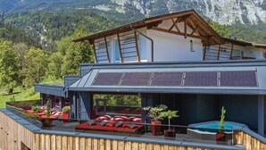A modern two-story building with a wooden deck, red outdoor seating, and a swimming pool. - Das Urgestein (Stans)