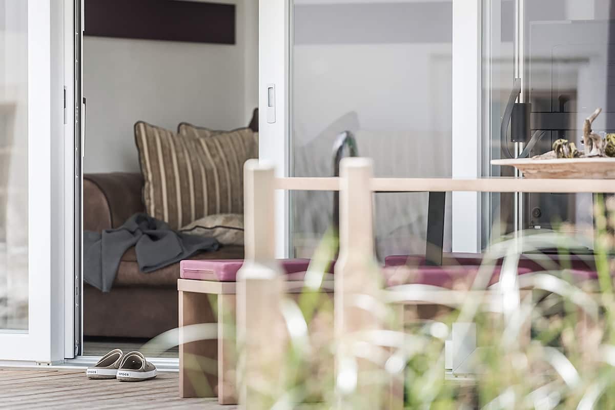 A modern living room with a glass door leading to a balcony, a wooden table, and a pair of shoes on the floor.