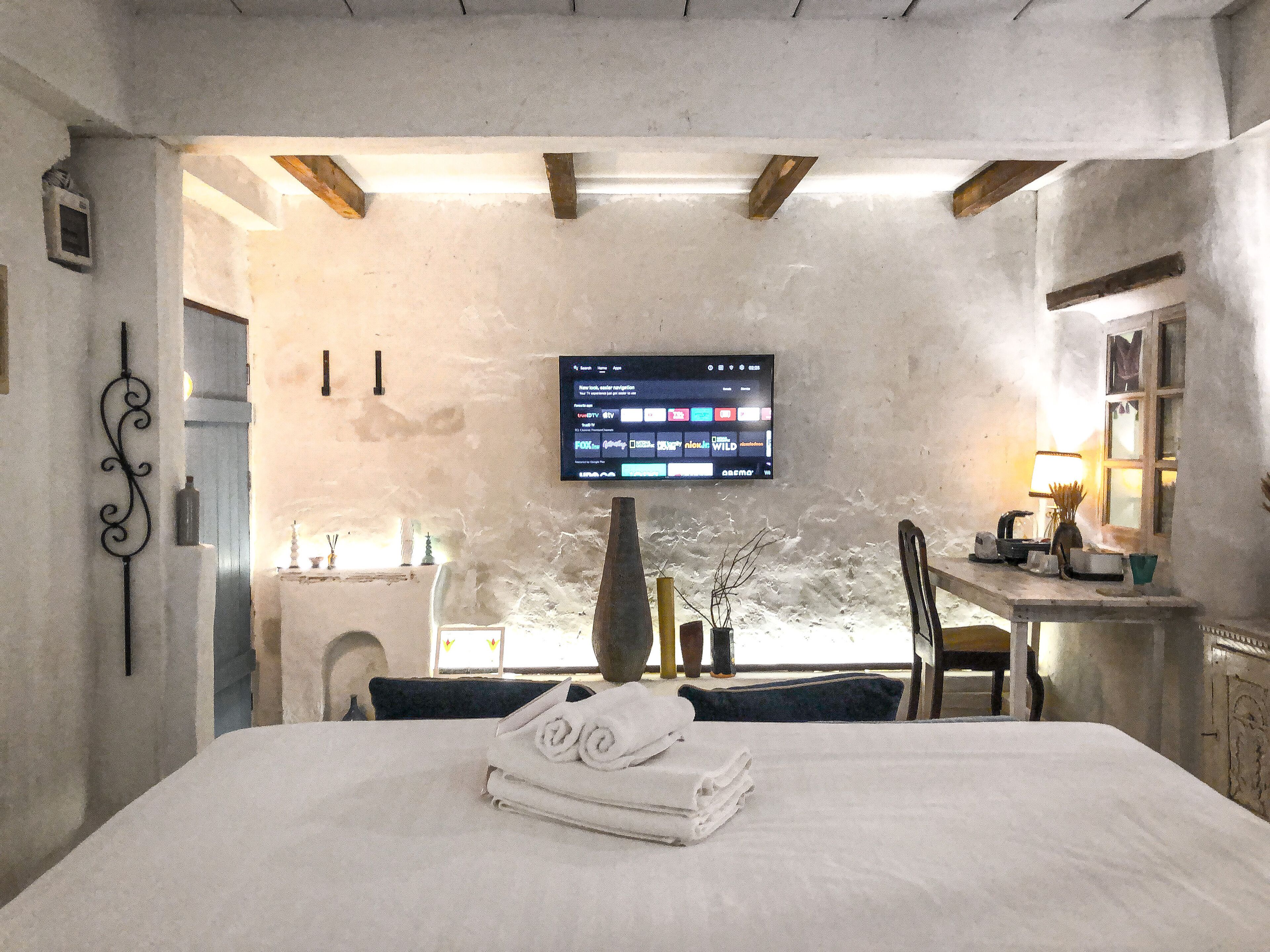 Ein Hotelzimmer mit Bett, Wandfernseher, Schreibtisch mit Lampe und Fenster.