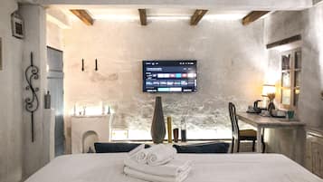 Una habitación de hotel con cama, televisión montada en la pared, escritorio con lámpara y ventana.