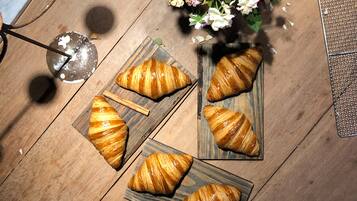 Una mesa de madera con cuatro croissants sobre tablas de madera rectangulares, un colador metálico y un ramo de flores.