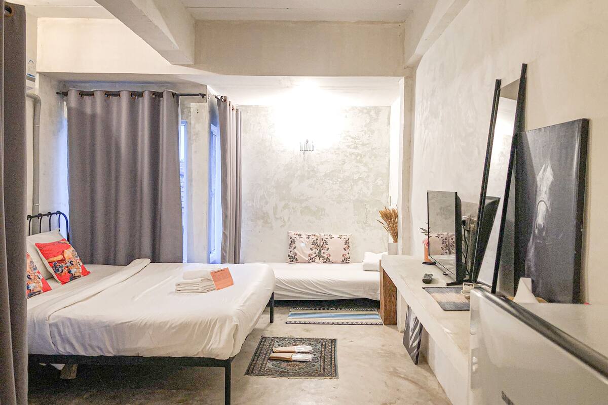 A bedroom with two beds, a desk, a mirror, and a TV.