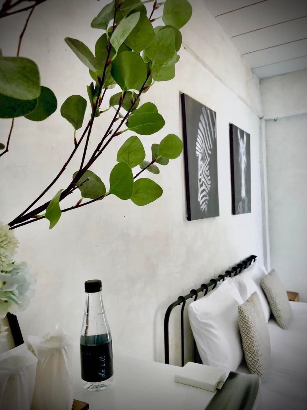 A room with a bed, a table with a bottle, and wall art.