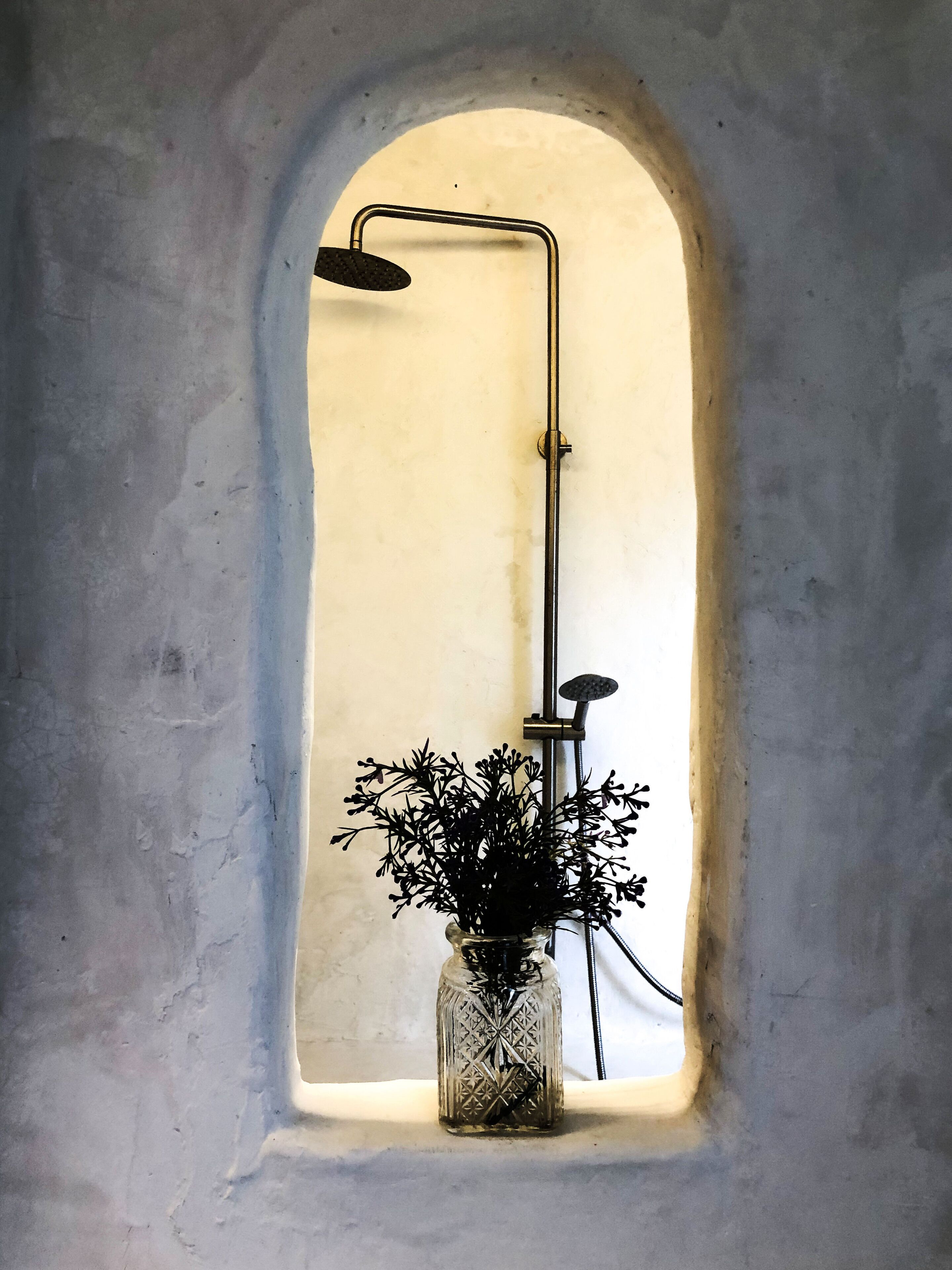 Una ducha con un florero de flores en una ventana.
