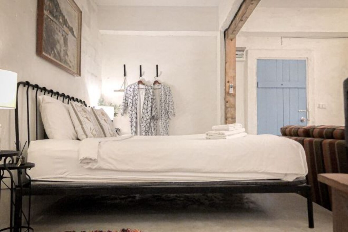 Un dormitorio con cama, una silla, una mesa y una puerta.
