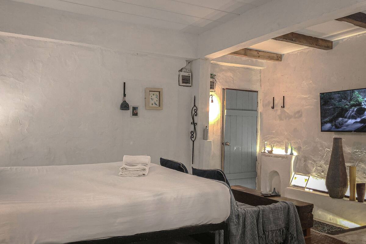 A bedroom with a bed, bedside table, lamp, and a television on the wall.