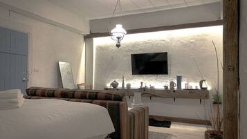 A bedroom with a bed, a bedside table, a mirror, a television mounted on the wall, and a shelf with decorative items.