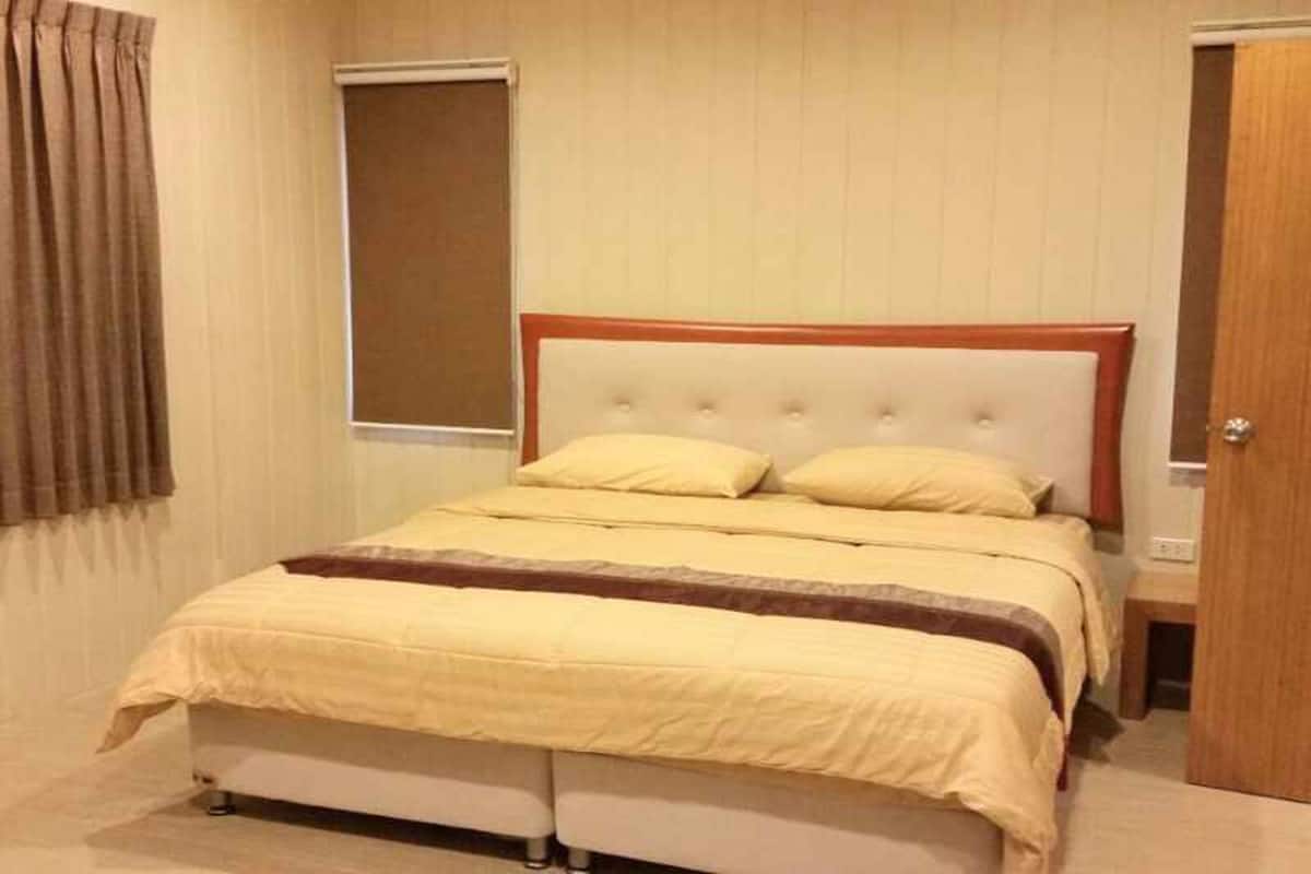 A neatly made bed with a white headboard and a brown accent, a wooden nightstand beside it, and a door to the right.