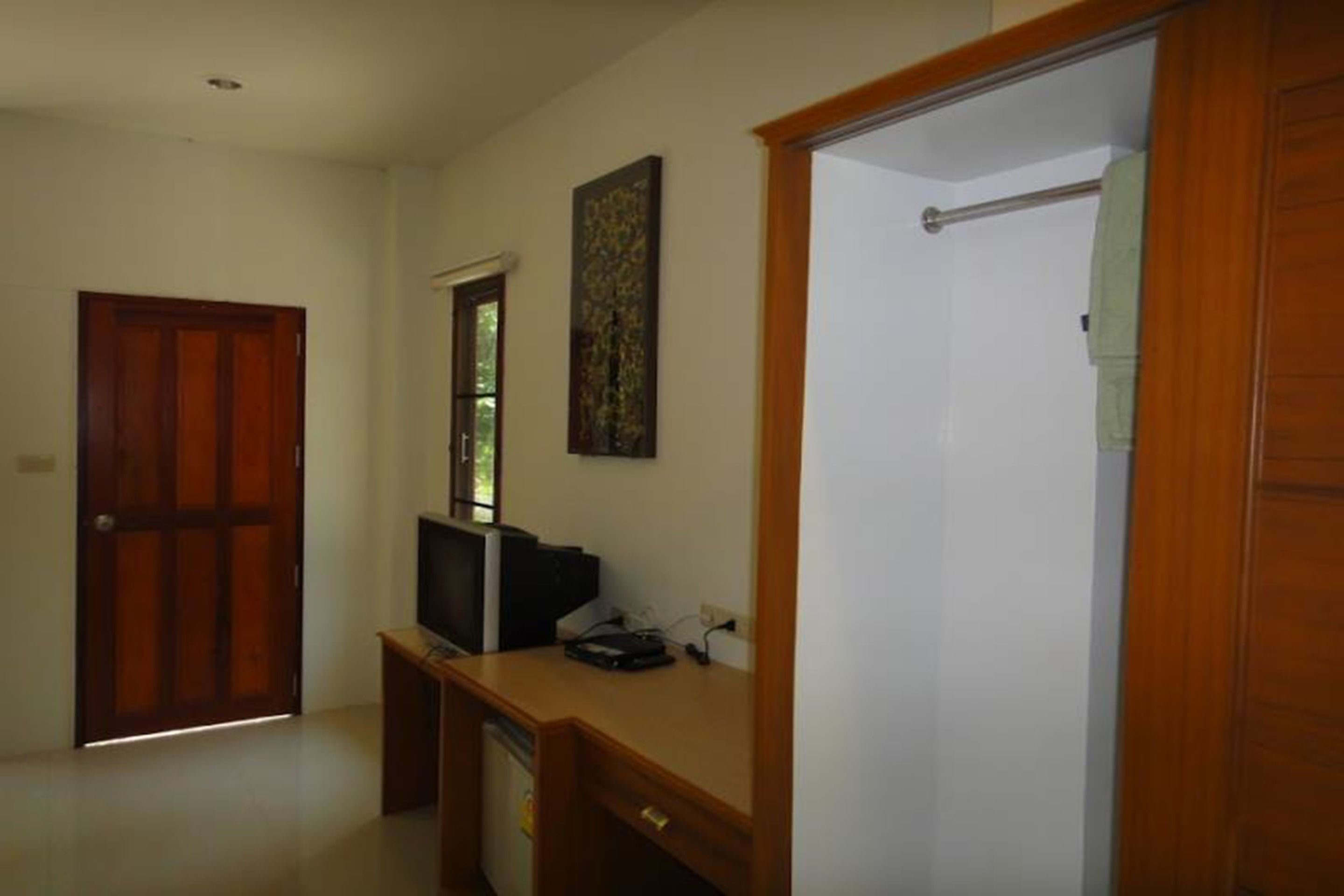 Ein Zimmer mit Holztür, Schreibtisch mit Computer, Fenster und einer Duschkabine.