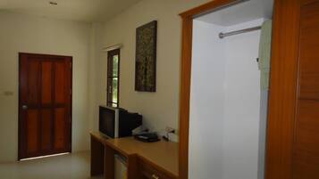 Ein Zimmer mit Holztür, Schreibtisch mit Computer, Fenster und einer Duschkabine.