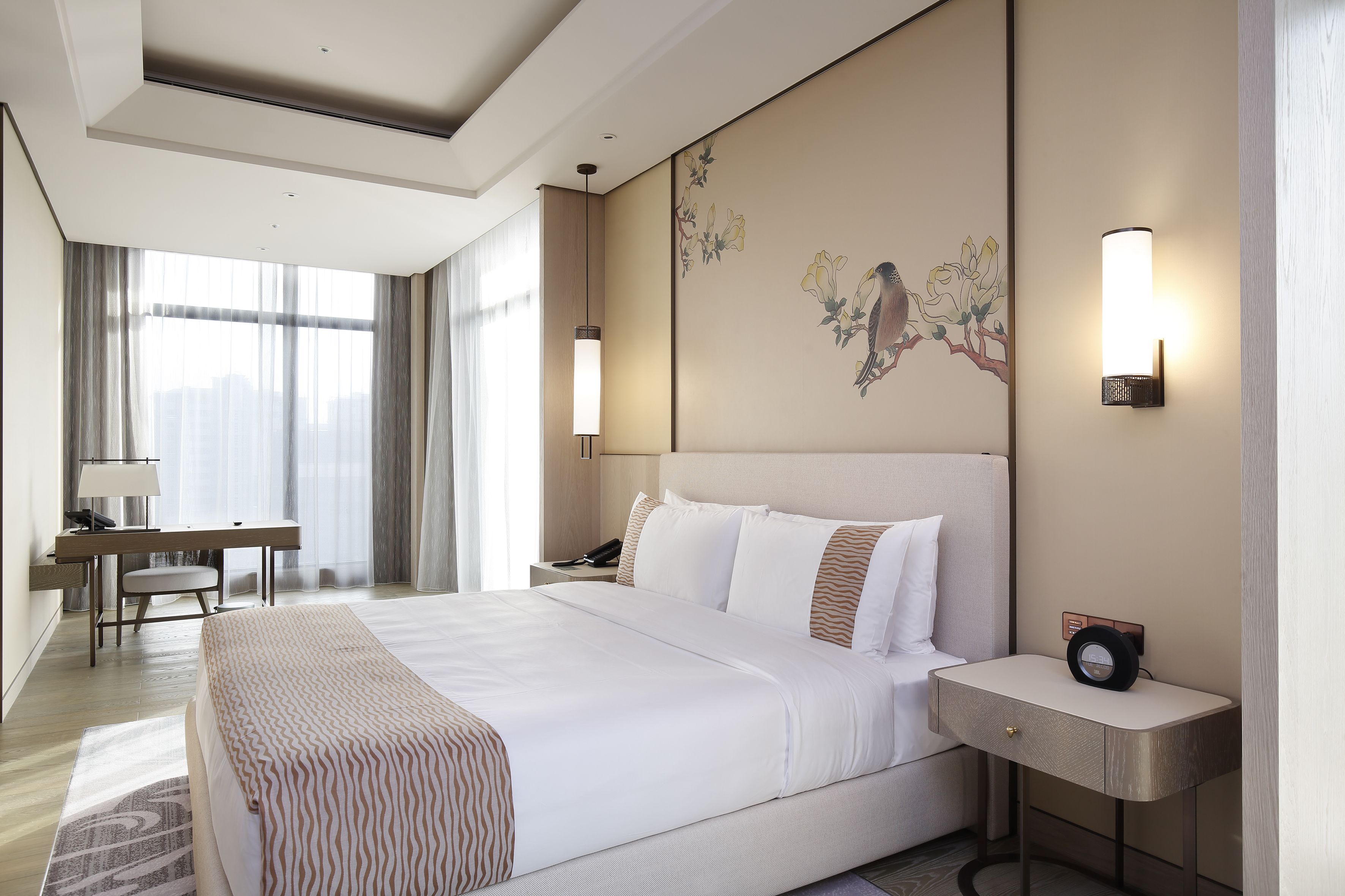 A modern hotel room with a large bed, bedside tables, a desk, and a chair.