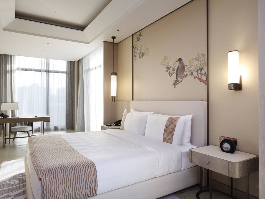 A modern hotel room with a large bed, bedside tables, a desk, and a chair.