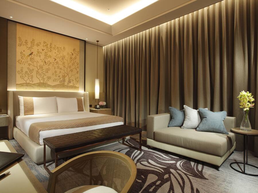 Una habitación de hotel con una cama grande, un sofá, una mesita, una silla y un panel decorativo en la pared.