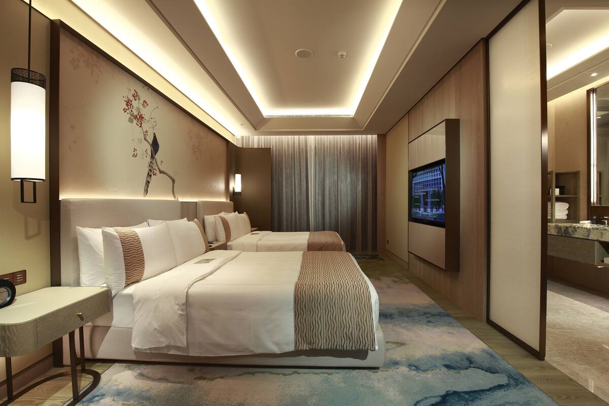 A hotel room with two beds, a TV, a large mirror, and a wall-mounted artwork.