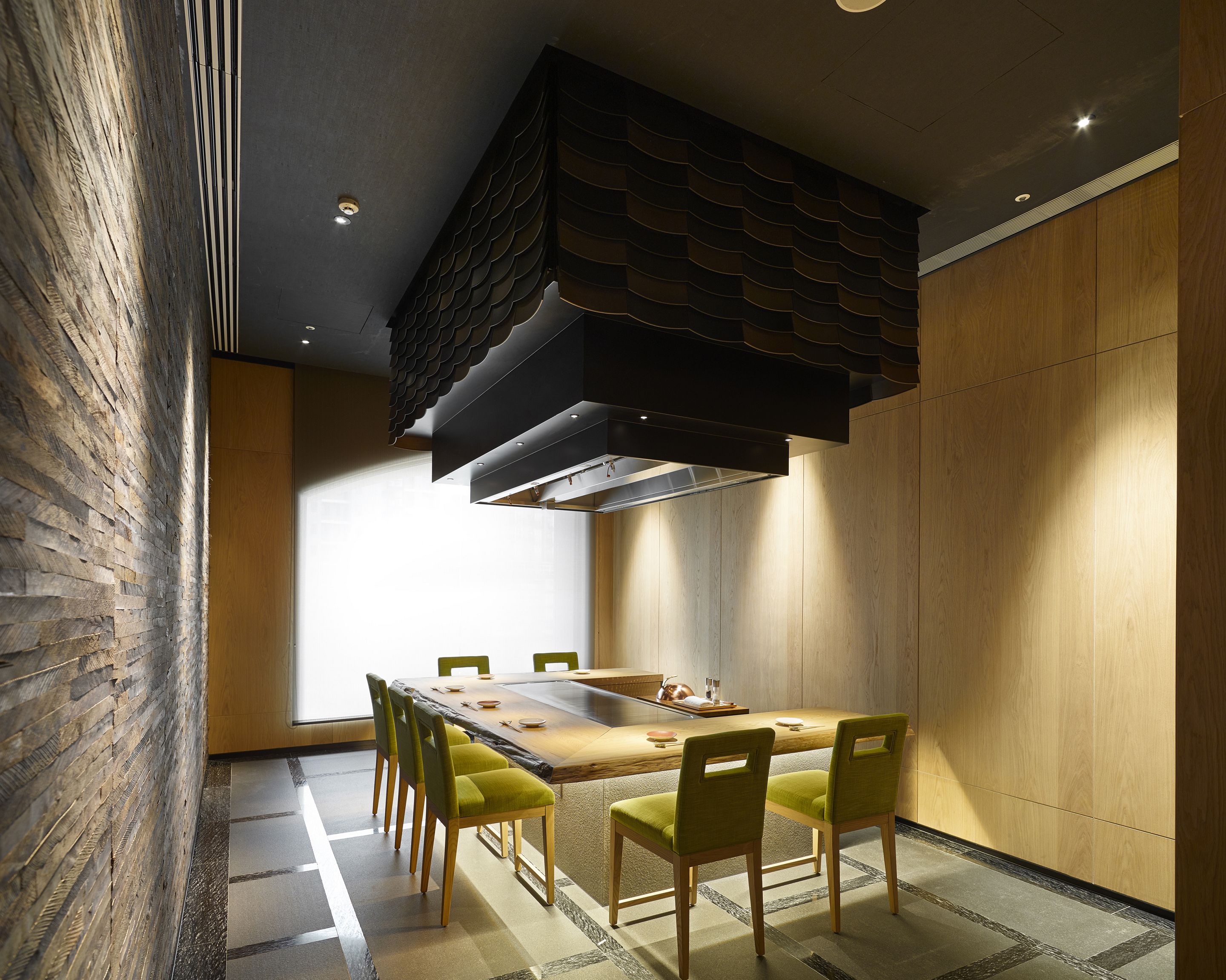 A modern dining area with a long table, green chairs, and a unique ceiling design.