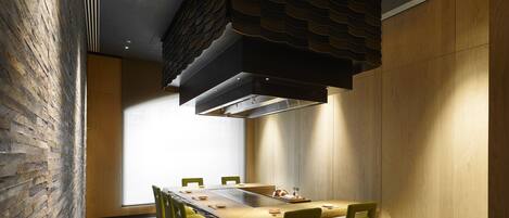 A modern dining area with a long table, green chairs, and a unique ceiling design.