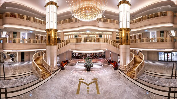 En hotellobby i flere etager med marmorgulv, en stor lysekrone og et centralt dekorativt element.