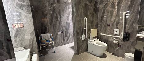 A modern bathroom with a marble wall, a toilet with a handrail, a wheelchair, and a shower area.