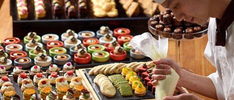 Un chef prépare des desserts à un buffet où diverses pâtisseries et autres douceurs sont présentées sur la table.