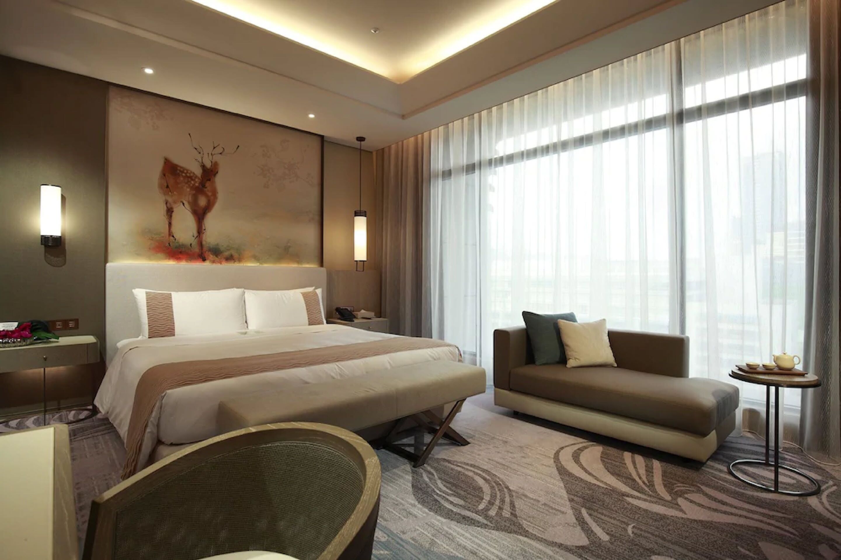 Una habitación de hotel moderna con una cama grande, un sofá, una mesita y un cuadro colgado en la pared.