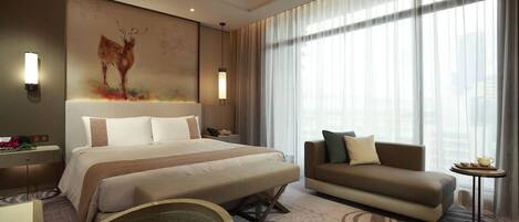 Una habitación de hotel moderna con una cama grande, un sofá, una mesita y un cuadro colgado en la pared.