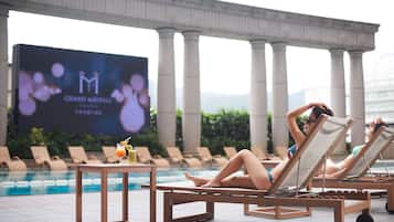 A poolside area with lounge chairs and a large screen displaying the Grand Mayfair logo.