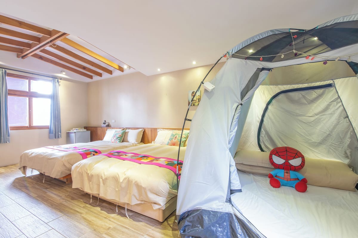 A bedroom with two beds, a tent, and a Spiderman plush toy.