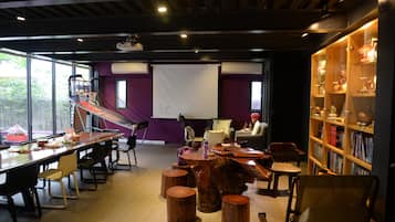 Ein moderner Konferenzraum mit langem Tisch, Stühlen, einer Projektionsleinwand und einem Bücherregal.