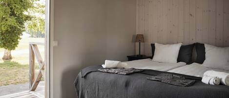 Een slaapkamer met een bed, een nachtkastje, een lamp en uitzicht op het groen.