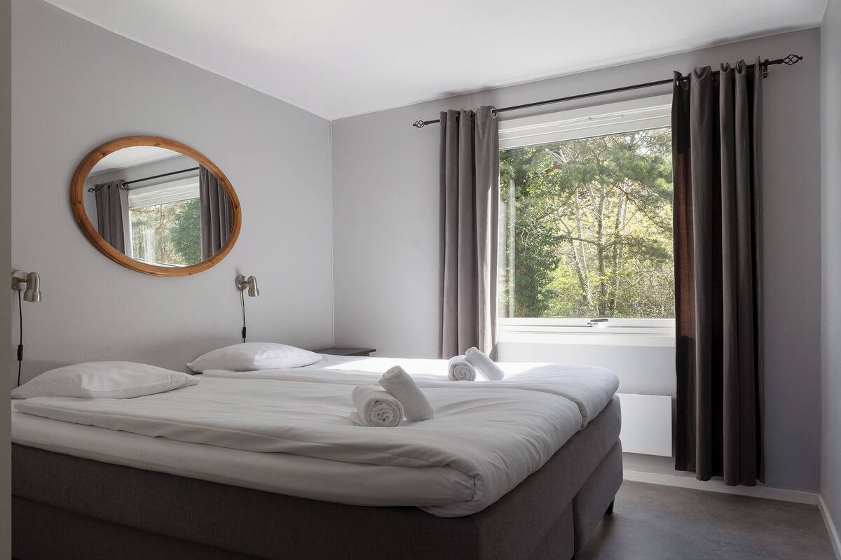 Une chambre avec un grand lit, un miroir rond et une fenêtre avec des rideaux.